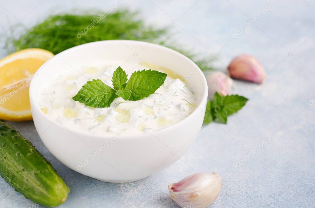 Greek dip sauce or dressing tzatziki decorated with olive oil and mint on blue background.