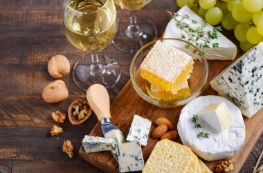 Ahşap bir masada üzüm, kraker, bal ve fındık ile Peynir tabağı.