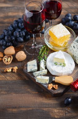 Ahşap bir masada üzüm, bal, fındık ve kırmızı şarap ile Peynir tabağı.