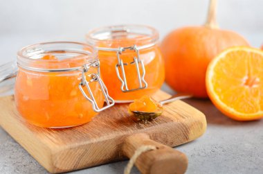 Ev yapımı balkabağı ve turuncu turuncu konfeksiyon gri beton arka planda kavanozlarda.