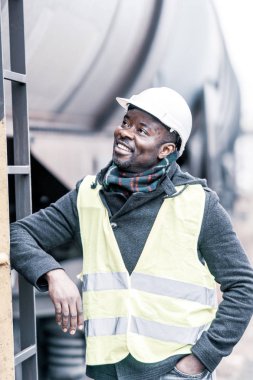 Gülümseyen ve memnun Afro-Amerikan Mühendisi Şantiye poz koruyucu iş giysisi giyen portresi