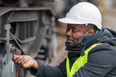 Güvenlik ekipmanı (kask ve ceket) giyen Afrikalı Amerikalı tamirci dişli trenini kontrol ediyor ve denetliyor