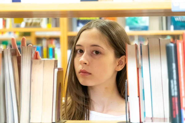Young female student looking for a book on the bookshelf in the school library