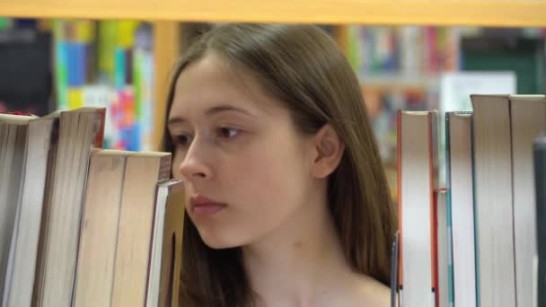 在学校图书馆的书架上找一本书的女学生 — 图库视频影像