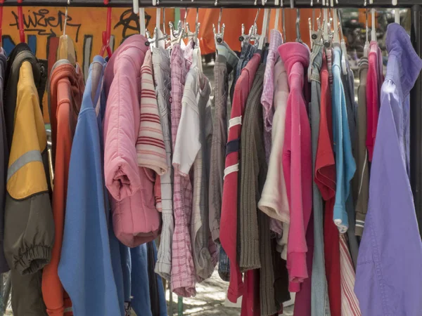 Colourful second-hand clothes and jackets hanging on a rack in a flea market