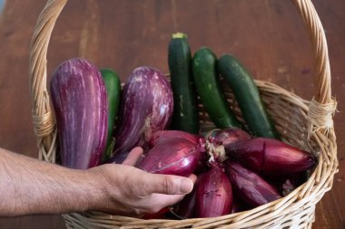 Patlıcan, kabak ve diğer arpacık soğanı dolu bir hasır sepetten bir arpacık soğanı almak