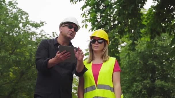 Two absorbed construction engineers, a man and a woman, wearing protective helmets inspecting the construction site using a digital tablet computer