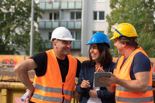 Senior foreman wearing safety vest, helmet and goggles providing instructions to a male and a female colleagues using a digital tablet computer on construction site