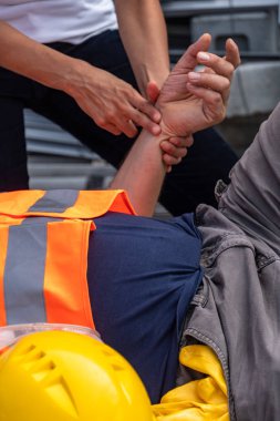 Bir sağlık görevlisinin ellerinin, işyerinde yaralanan bir inşaat işçisinin nabzını kontrol eden görüntüsü kırpılmış