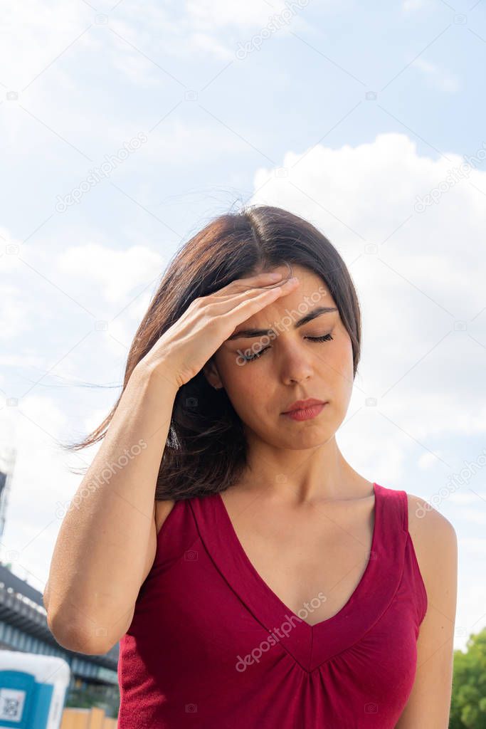 Close up portrait of a brunette woman dealing with an awful headache. Outdoors