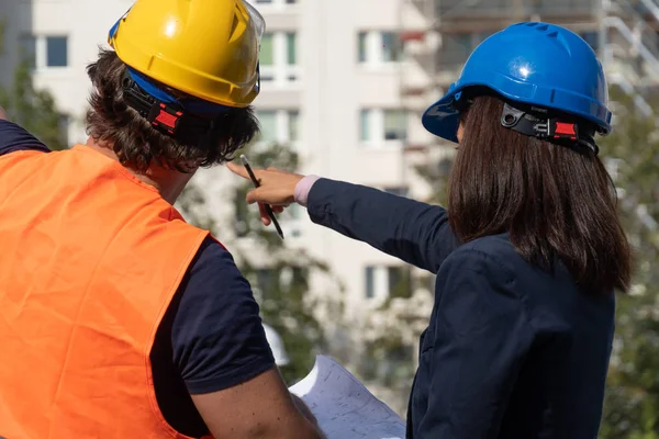 Back turned female engineer at work on construction site with a foreman wearing a safety jacket and a protective helmet