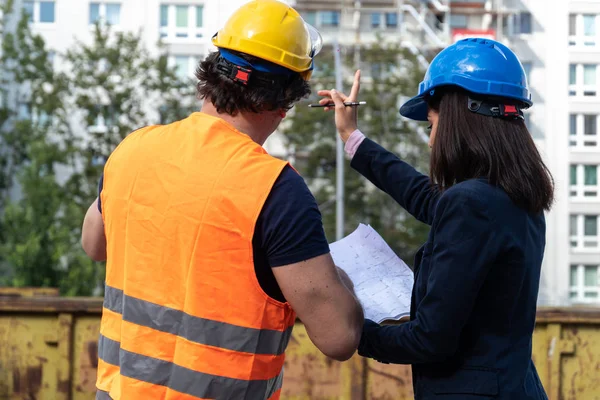 Back turned female engineer at work on construction site with a foreman wearing a safety jacket and a protective helmet