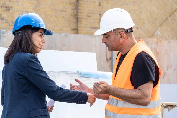 Female construction boss talking to a foreman. Profile. Outdoors
