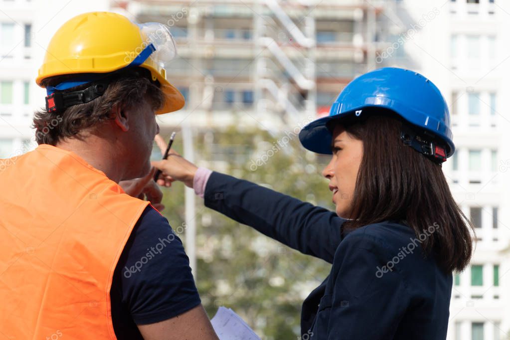 Back turned female engineer at work on construction site with a foreman wearing a safety jacket and a protective helmet