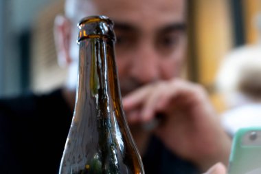 Pensive ve üzgün adam üzüntülerini bir şişe birada boğuyor. Ön planda bira şişesi üzerinde seçici odak