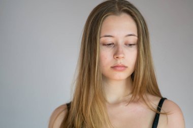 Gri arkaplanda somurtkan bir yüzü olan güzel ve düşünceli genç bir kadının portresini yakından çek.