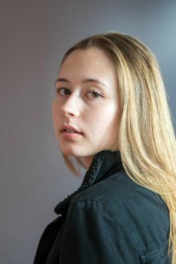 Uzun doğal sarı saçlı ve kameraya bakan pürüzsüz tenli güzel bir genç kızın yarı profil portresi. Stüdyo çekimi