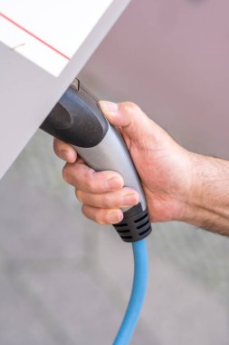 Bir adam elinde elektrikli araç şarj konnektörü tutuyor.