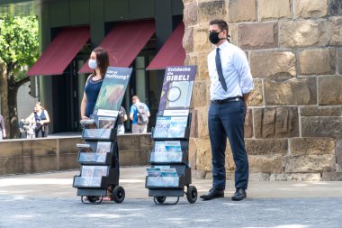 Heilbronn, Germany - July 10, 2020: Jehovah's Witnesses standing next to their books and pamphlets wearing medical protective masks clipart
