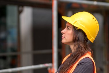 Çekici bir kadın fabrika işçisinin profil portresi sarı bir kask takıyor ve yan bakıyor.
