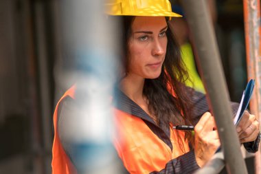 Güvenlik kaskı ve yelek giyen kadın inşaat mühendisi ofis planlarını kontrol ediyor. 