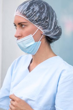 Tıbbi başlık takan ve burnunu kapatmadan ameliyat maskesi takan bir doktorun profil portresi.