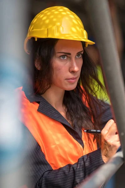 安全ヘルメットとベストチェックオフィス設計図を身に着けている吸収女性土木技術者 — ストック写真