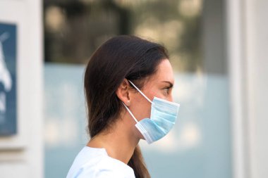 Yüzünü cerrahi koruyucu bir maskeyle örten bir sağlık çalışanının profil portresi.