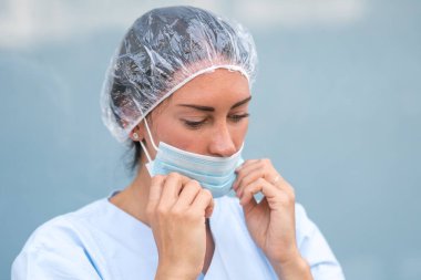 Cerrahi koruyucu maskesini takan bir doktorun portresi.