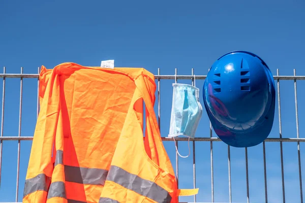 Occupational safety and protection against adverse conditions at work. Blue hard hat, reflective vest and protective surgical mask hanging on scaffolding