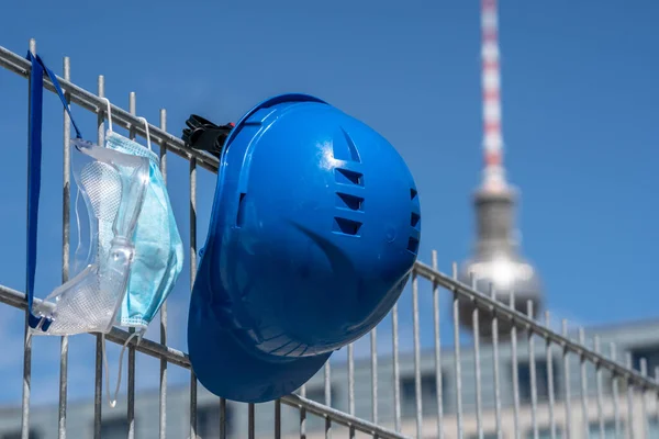 Occupational safety and protection against adverse conditions at work. Blue hard hat and protective surgical mask hanging on scaffolding. On background out of focused Berlin landmark television tower