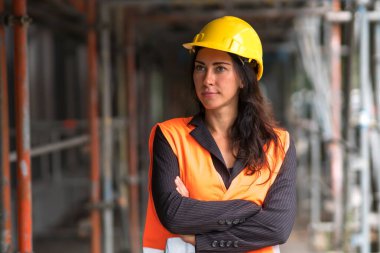 Çekici bir kadın inşaat müdürünün portresi koruyucu bir kask takıyor ve güvenlik yeleği katlanmış kollarla dışarıda poz veriyor.