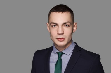 Sıradan yakışıklı bir genç adam. Kravatlı ve takım elbiseli, gri arka planlı, kendine güvenen beyaz bir adam..
