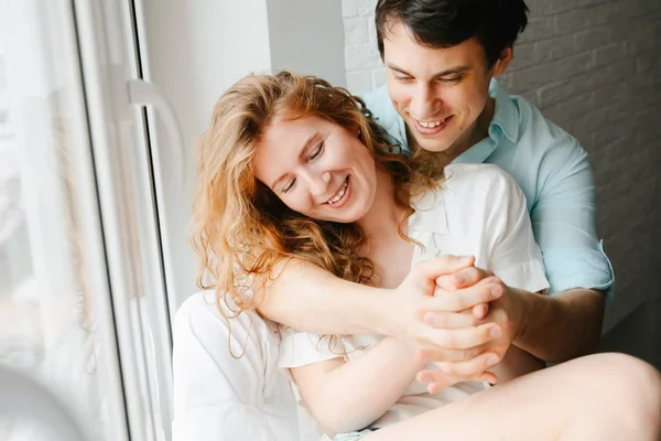 Happy girl and man hugging near window in home. — Stock Photo, Image
