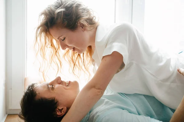Menina feliz e homem abraçando perto da janela em casa. Roupas brancas e azuis. Dia dos namorados . — Fotografia de Stock