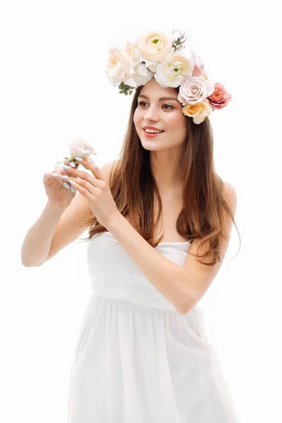Mooi jong meisje glimlachend en poseren met bloemen op witte achtergrond in witte jurk. Studio portret. — Stockfoto