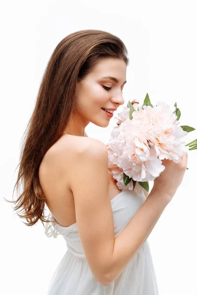 肖像美丽的年轻女孩微笑和摆姿势与人造花在白色背景在白色礼服. — 图库照片