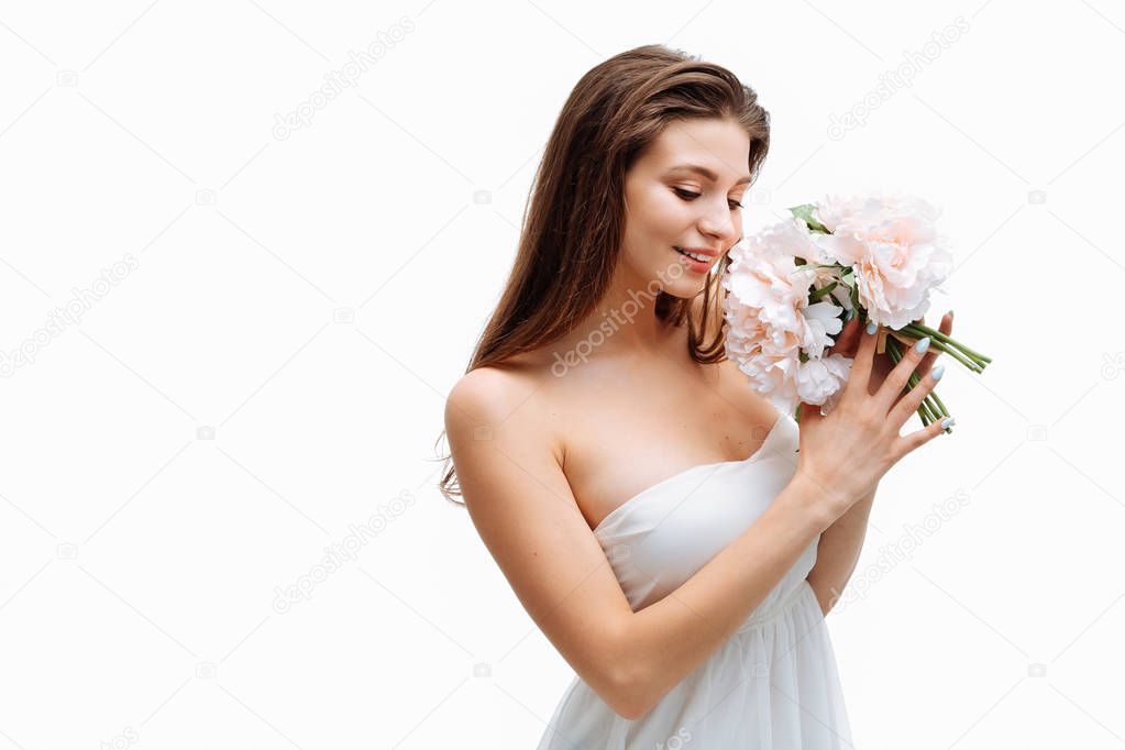 Portrait beautiful young girl smiling and posing with artificial flowers on white background in white dress.