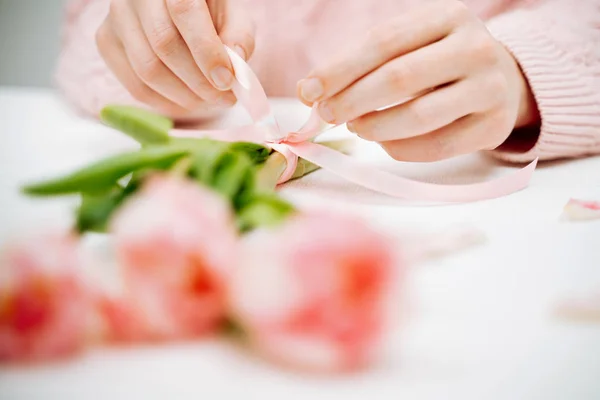 Mujer joven atando una cinta en un ramo de tulipanes rosados . — Foto de Stock