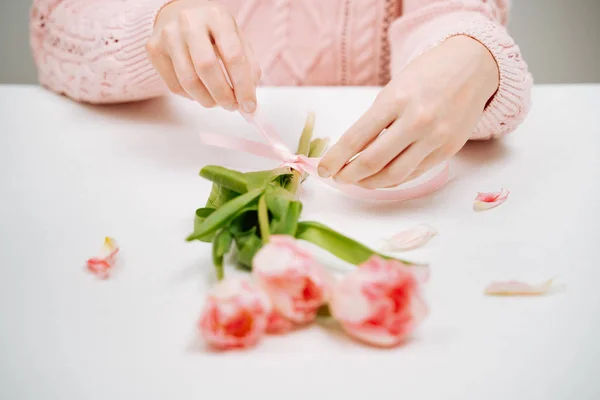 Mujer joven atando una cinta en un ramo de tulipanes rosados . — Foto de Stock