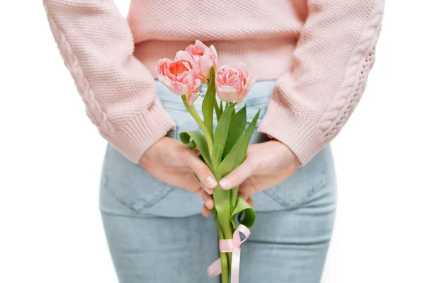 Mujer joven sosteniendo tulipanes rosados detrás de su espalda sobre un fondo blanco . — Foto de Stock