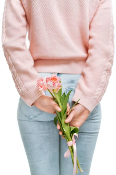 Mujer joven sosteniendo tulipanes rosados detrás de su espalda sobre un fondo blanco . — Foto de Stock