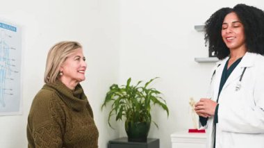 Çeşitli bir kadın doktor ve hastası beşlik çakıyor, olumlu bir tıbbi danışma sırasında neşe ve başarı anlarını paylaşıyorlar. Bu, mükemmel sağlık hizmetleri, karşılıklı güven ve olumlu sağlık sonuçlarını temsil etmektedir..