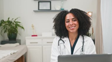 Dost canlısı bir kadın doktor gülümseyerek çevrimiçi tıbbi konsültasyon sağlıyor. Çağdaş dijital sağlık hizmetleri ve erişilebilir bakımı temsil eden profesyonel sağlık hizmeti ve sanal destek sunmaktadır..