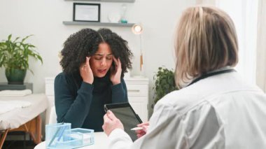 Çeşitli bir kadın, modern bir klinikte tıbbi konsültasyon sırasında ilgili bir kadın doktorla sağlık sorunlarını paylaşıyor. Doktor dikkatle dinliyor, profesyonel sağlık hizmeti sunuyor..