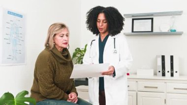 Profesyonel ve çeşitli bir kadın doktor, parlak ve temiz bir klinikte yaşlı bir hastaya kapsamlı bir tıbbi danışmanlık yapar. Önemli sağlık bilgileri ve tedavi planlarını dikkatle tartışırlar..