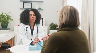 Beyaz önlüklü profesyonel ve çeşitli bayan bir doktor klinikteki yaşlı bir hastaya danışıyor. Doktor ve hasta arasındaki şefkatli sağlık hizmetleri ve açık iletişimi vurgulayan önemli bir tıbbi tartışmaya girişirler..