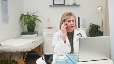 Olgun bir kadın doktor, ofisinden profesyonel tıbbi danışmanlık hizmeti sunar. Bu yetenekli hekim modern teknolojiyi verimli, merhametli sanal sağlık hizmetleri için kullanıyor, çeşitli hastalara hizmet ediyor..