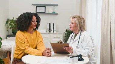 Şefkatli bir kadın doktor, klinik ortamındaki genç ve çeşitli bir hastaya profesyonel tıbbi danışmanlık sağlar. Randevu sırasında sağlık, güven ve net iletişim konularında dostça bir tartışmaya girişirler..