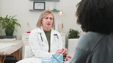 Beyaz önlüklü şefkatli bir kadın doktor, farklı bir hastayla dikkatle görüşüyor ve temiz, modern bir muayenehanede sağlık sorunlarını tartışıyor. Bu profesyonel değiş tokuş sağlık ve hasta sağlığını ön plana çıkarıyor..